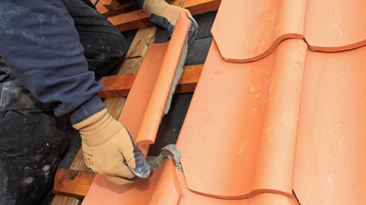 Ouvrier installant des tuiles orange à l'aide d'un outil manuel sur un toit en tuiles