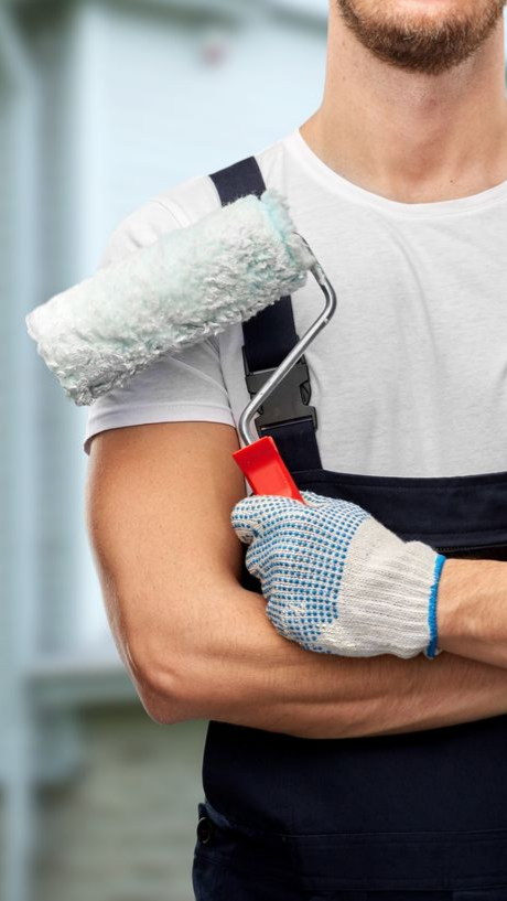 Peintre tenant un rouleau à peinture et un grattoir rouge, vêtue d'une salopette noire
