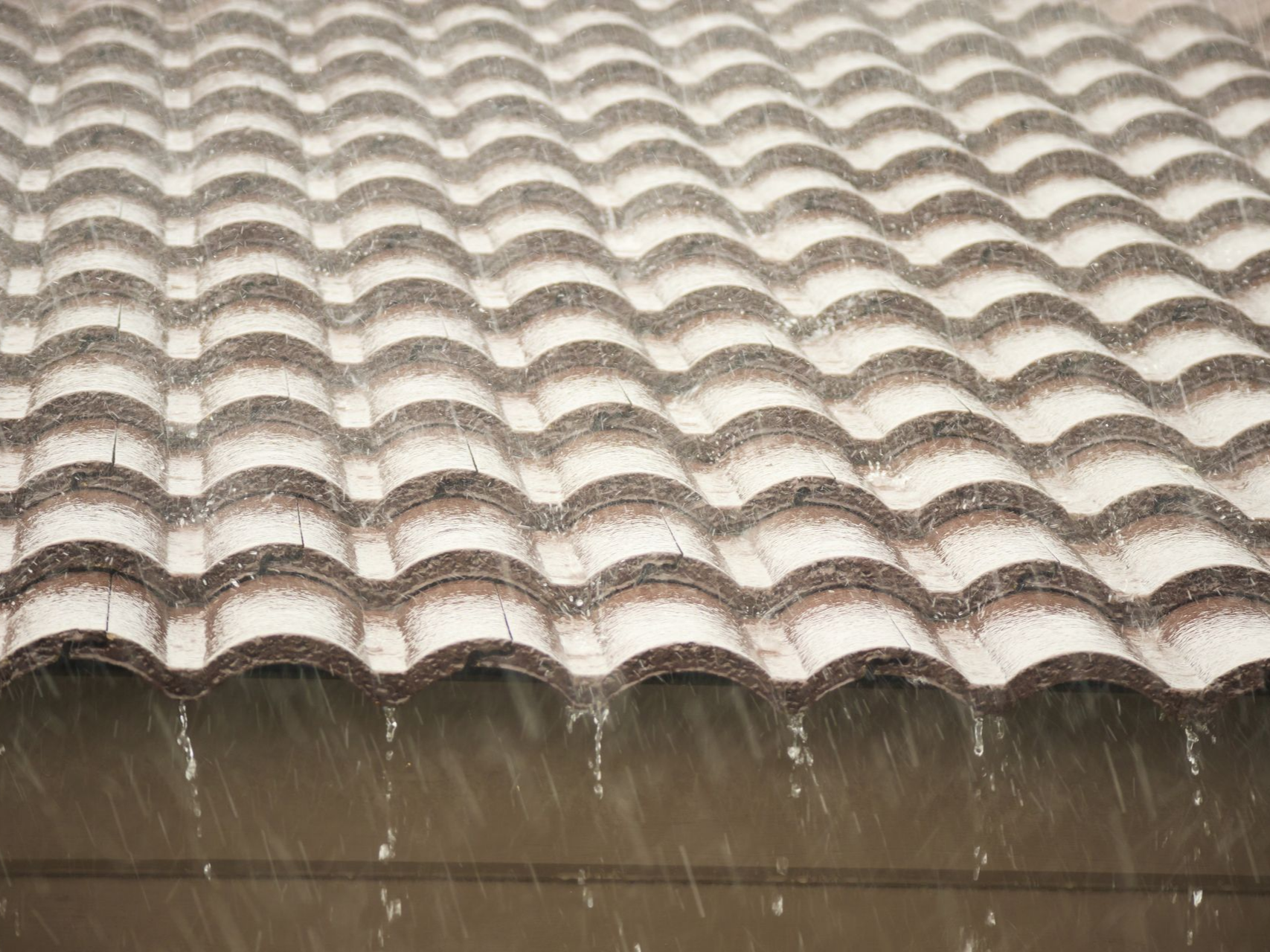 L'eau de pluie ruisselle d'un bord de toit festonné sur une surface humide