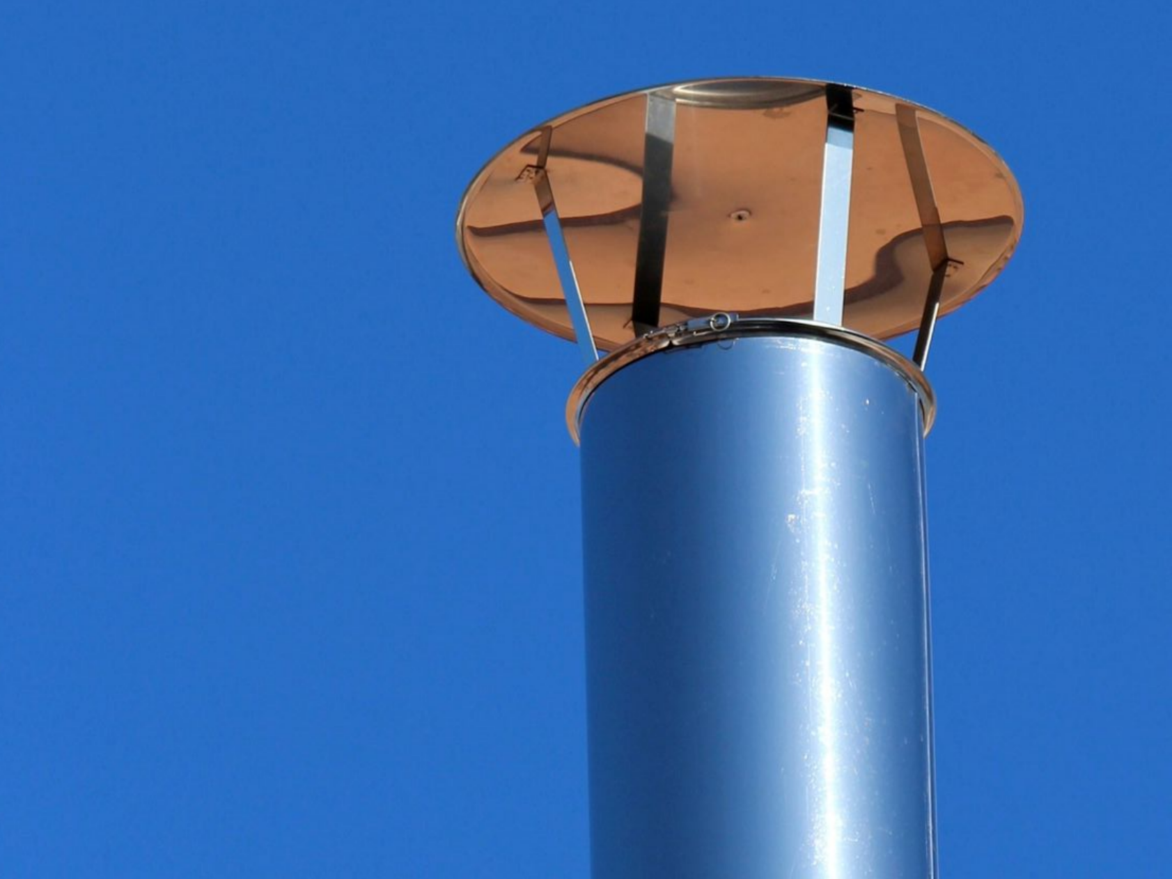 Tuyau de cheminée bleu avec un chapeau couleur rouille sur un ciel bleu clair