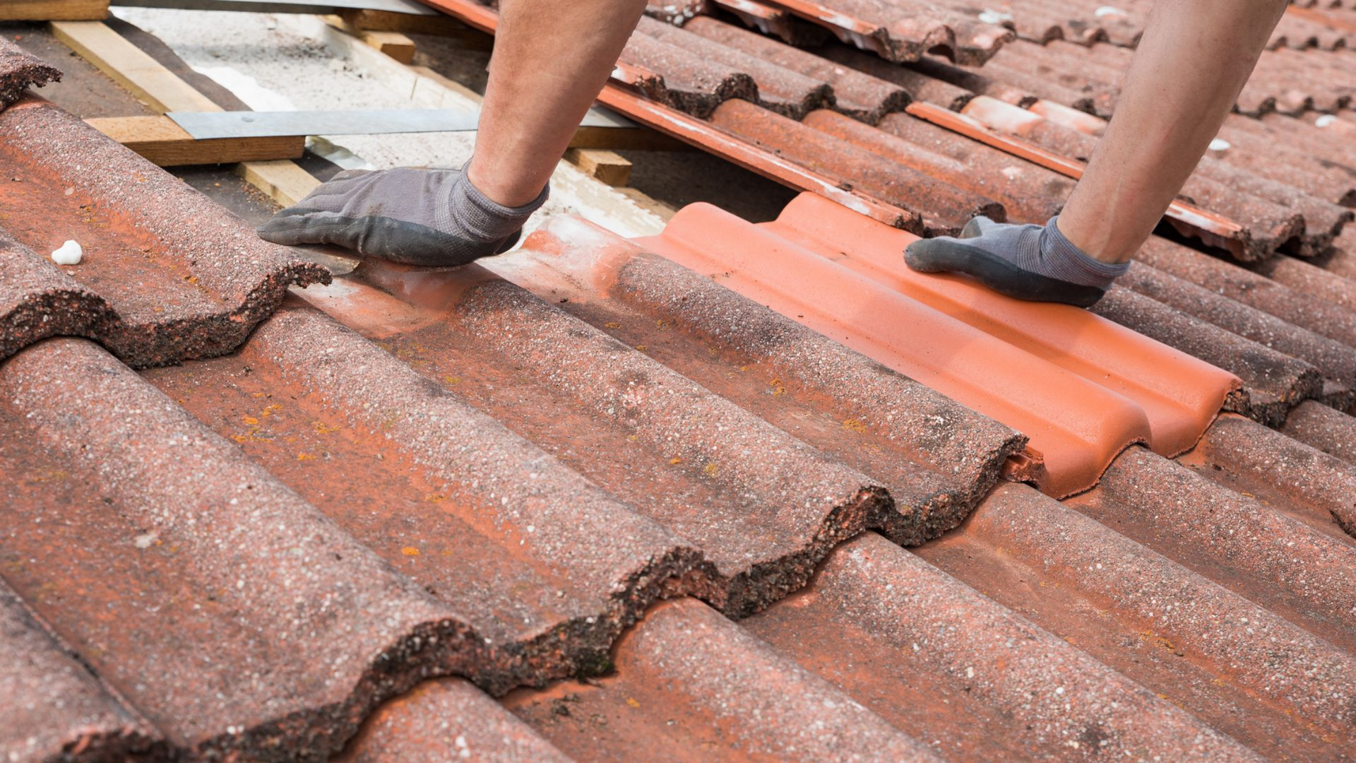 Des ouvriers gantés installent des tuiles orange sur un toit en pente et usé par les intempéries