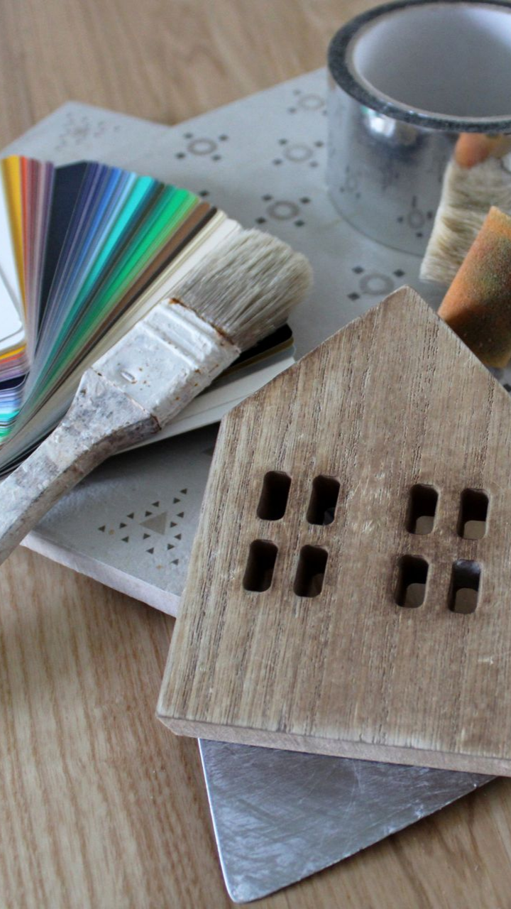 Des échantillons de peinture, un pinceau et deux petites maquettes de maisons en bois sur une table