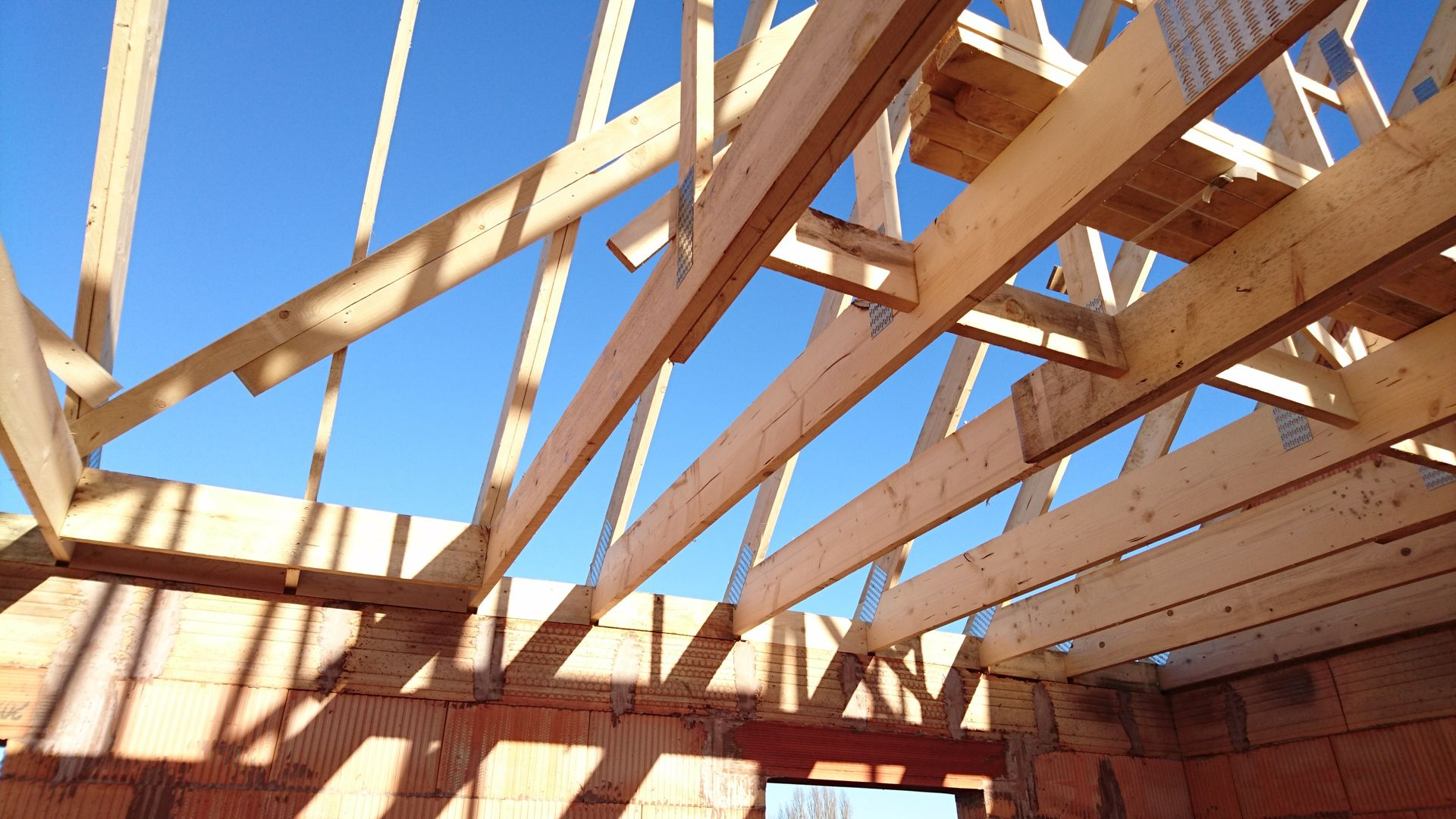 Charpente de toit en bois en construction sur fond de ciel bleu, avec des murs de briques en dessous