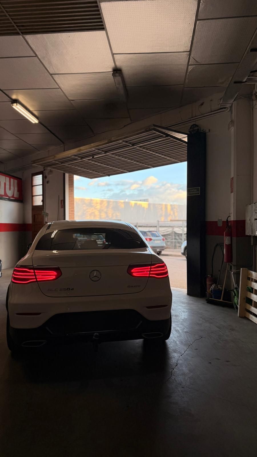 Un sedán blanco estacionado dentro de un garaje con la puerta abierta y montañas visibles desde el exterior.