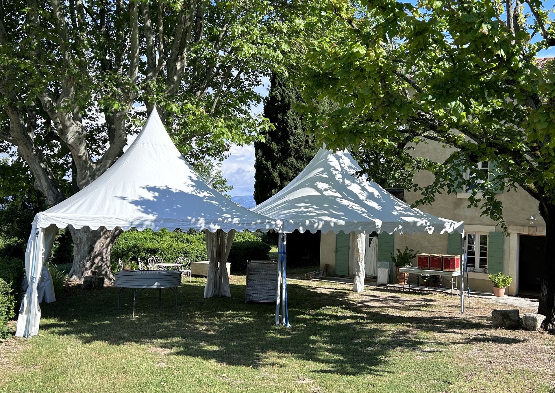 Deux tentes blanches sur une pelouse, avec des arbres et un bâtiment en arrière-plan.