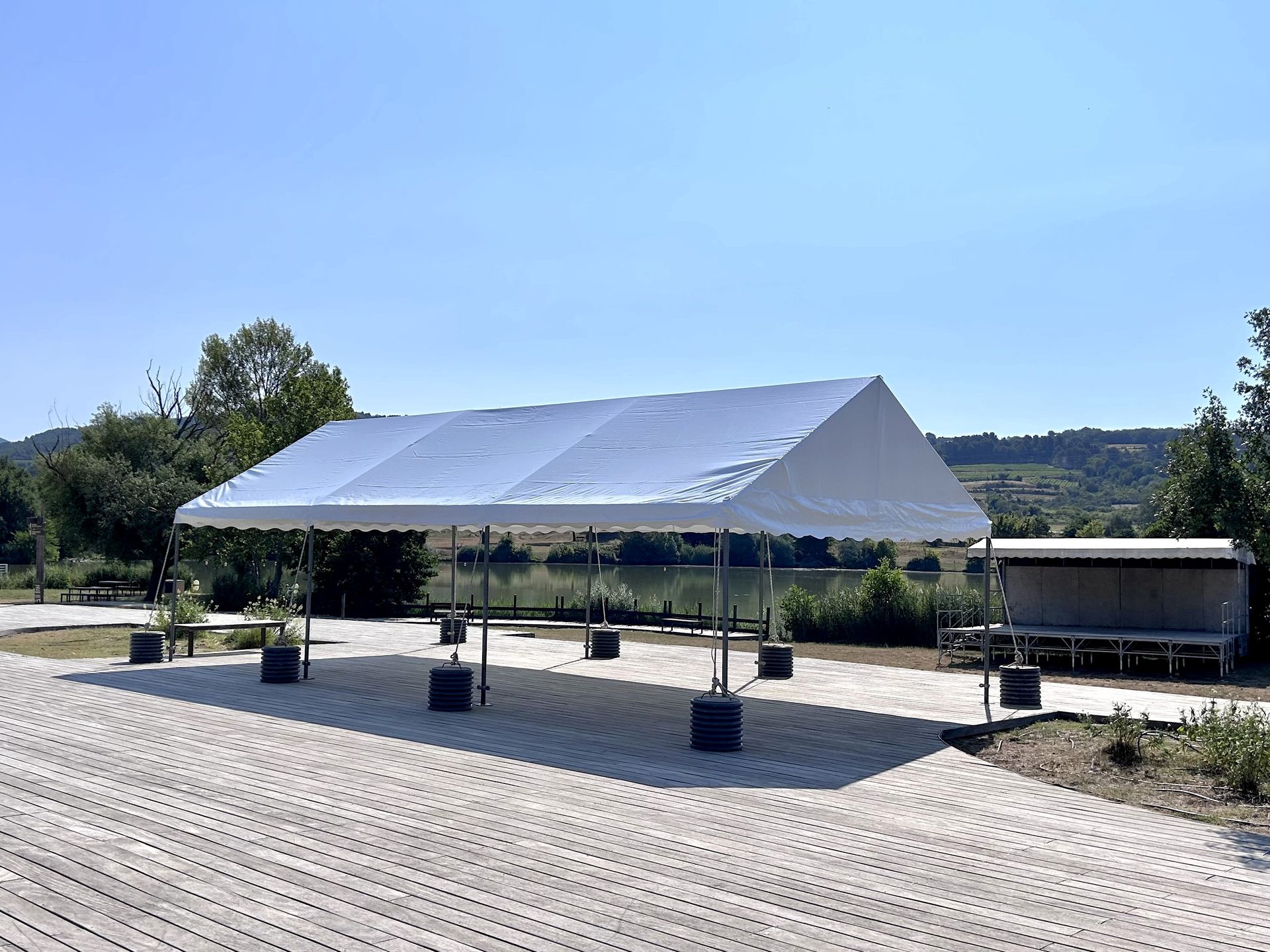 Une structure de tente blanche sur une aire pavée, avec des arbres en arrière-plan.