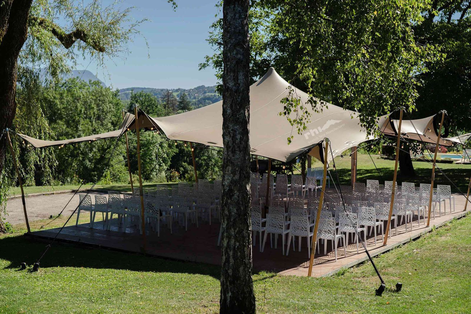 Aménagement d'un événement en extérieur avec des rangées de chaises blanches sous une tente stretch tendue.