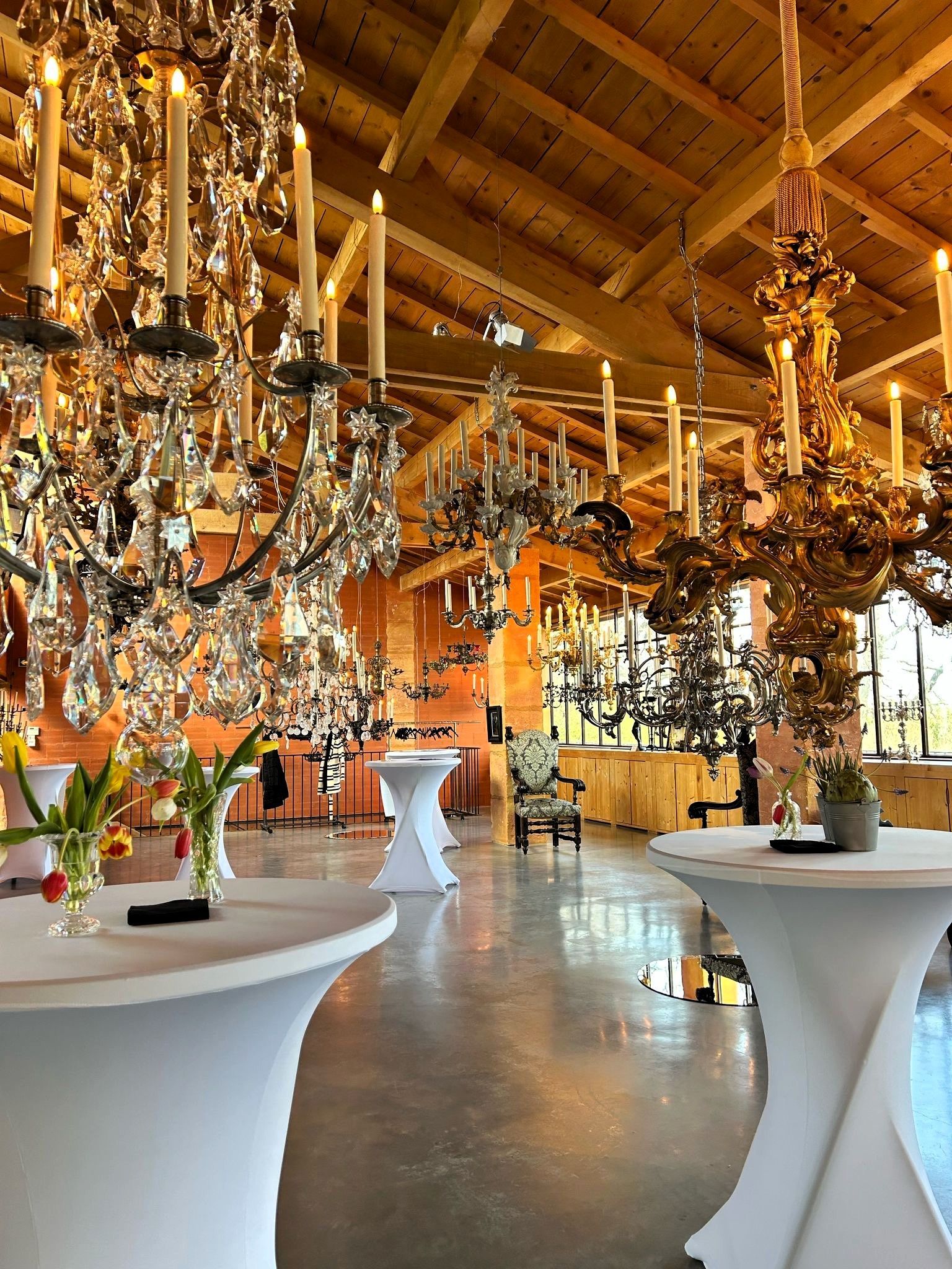 Un espace événementiel avec de multiples lustres surplombant des tables de cocktail nappées de blanc.