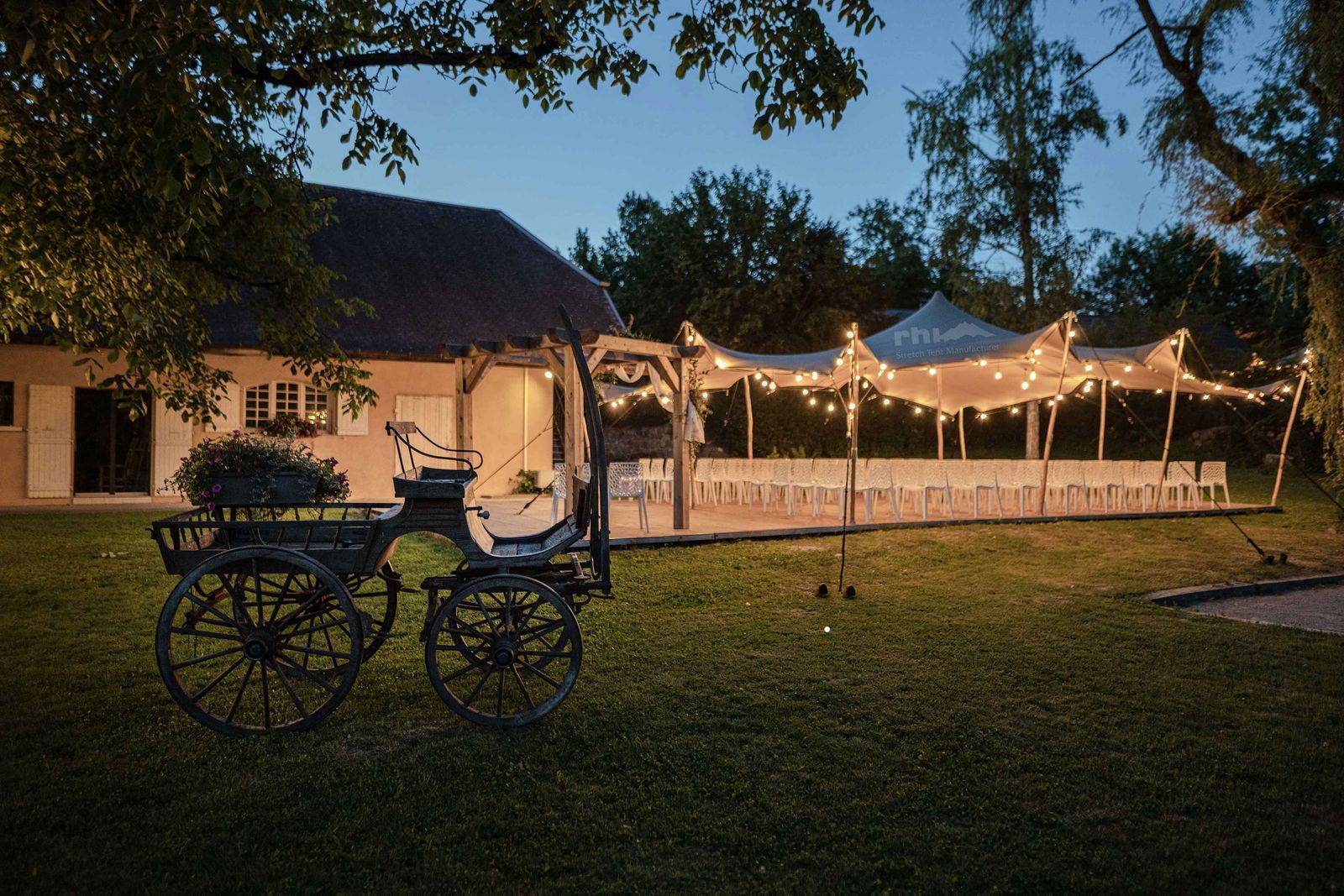 Calèche devant un bâtiment illuminé de guirlandes lumineuses sur une pelouse au crépuscule.