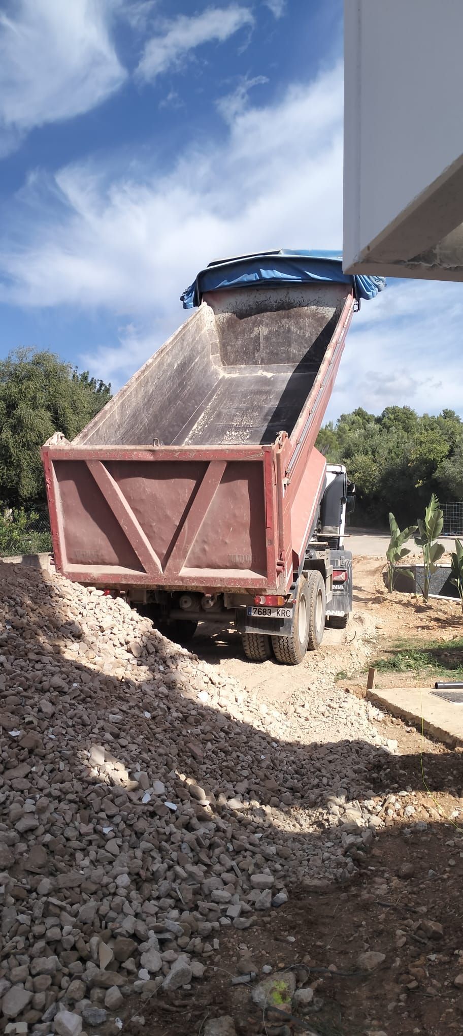 Camión volquete descargando rocas junto a una obra en construcción bajo un cielo azul.