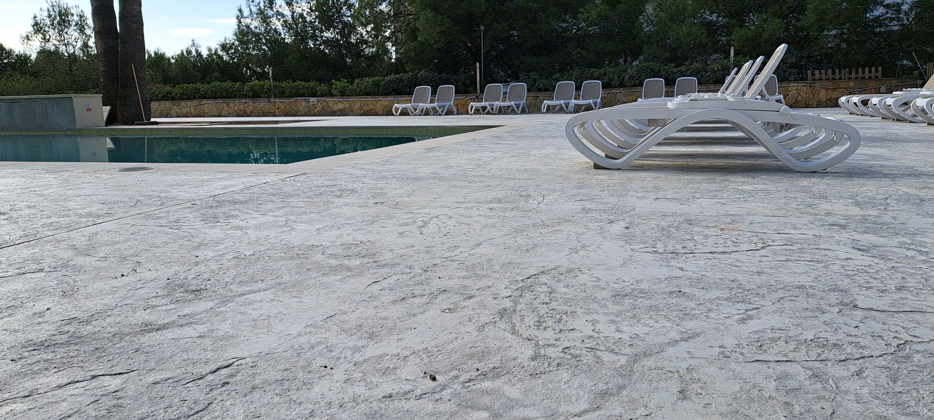 Un estrecho sendero exterior con grandes losas de piedra junto a una pared blanca y un borde de jardín plantado.