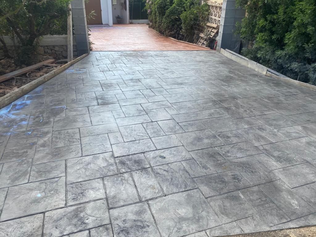 Un camino de entrada de hormigón que conduce a una casa con árboles al costado.