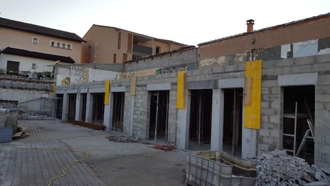 Une rangée de garages en blocs de béton en construction, avec des panneaux de coffrage jaunes sur les piliers, sur un chantier extérieur.