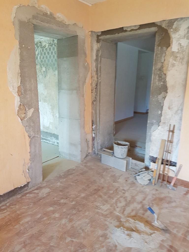 Un chantier de construction montrant deux ouvertures de porte dans un mur couleur pêche, avec du plâtre apparent, du mortier et des outils au sol.