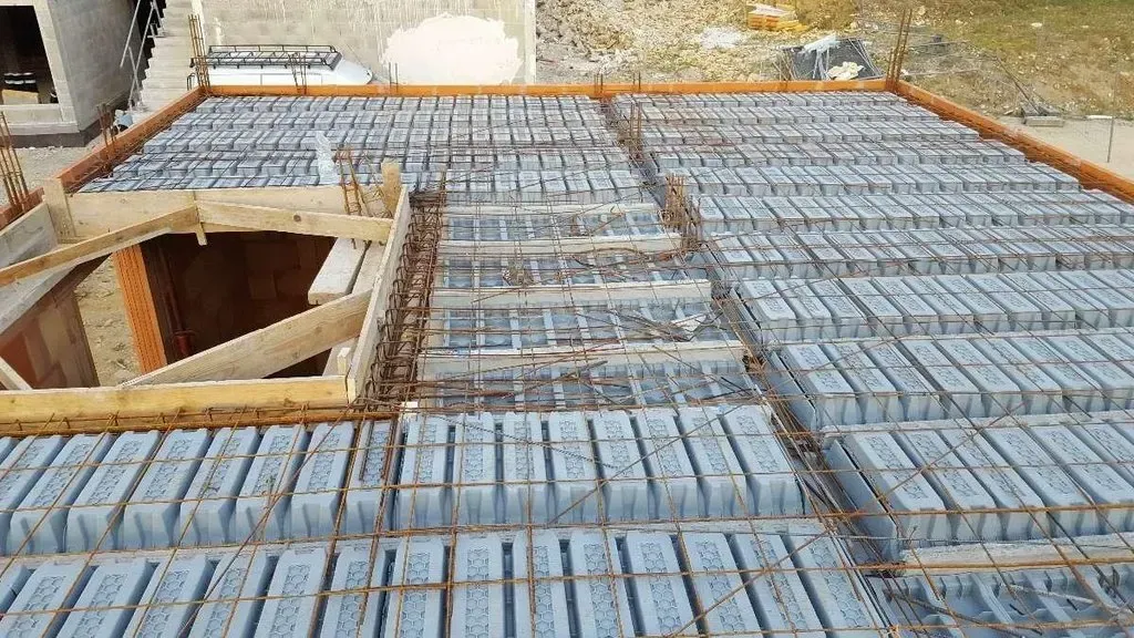 Chantier de construction montrant la pose d'une dalle de plancher avec des solives en béton, des blocs et un treillis d'armature en acier.