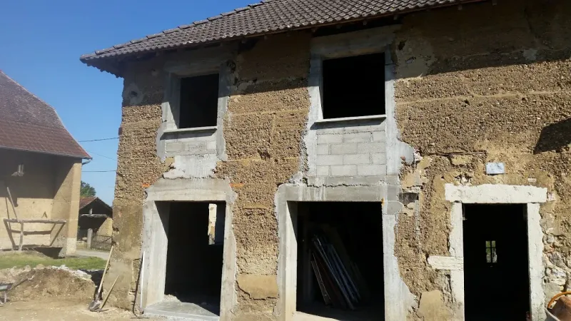 Un bâtiment d'un étage en construction, avec des murs en parpaings, des encadrements de portes et de fenêtres en béton et un toit de tuiles.