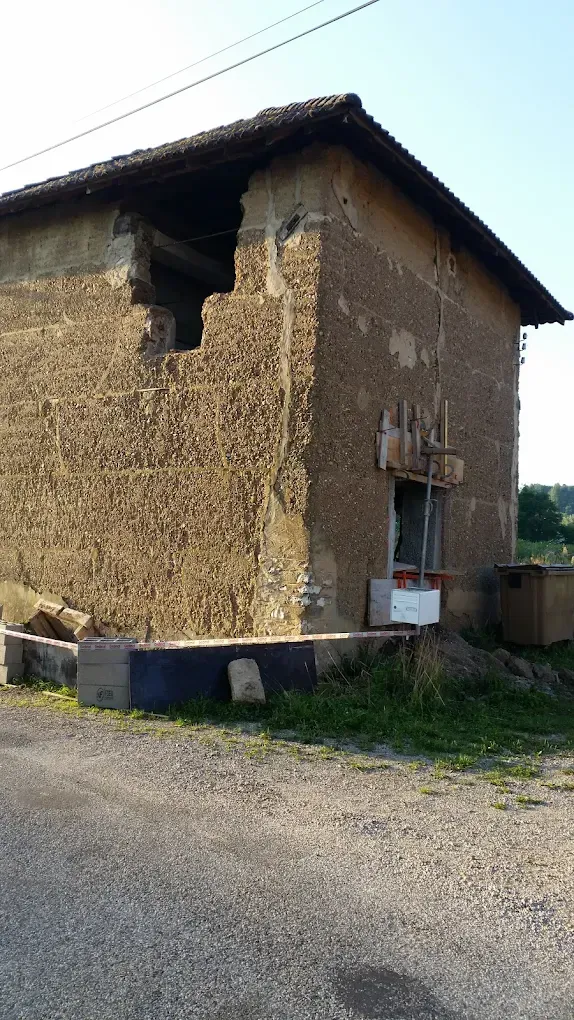 Un bâtiment, usé par le temps et partiellement en ruine, se dresse au bord d'un chemin de gravier sous un ciel d'un bleu limpide.