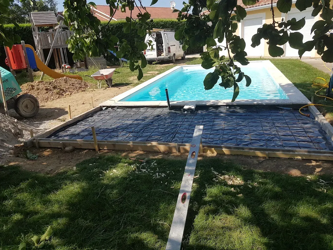 Une terrasse arrière partiellement construite, renforcée par une grille d'armature métallique, jouxte une piscine rectangulaire enterrée.