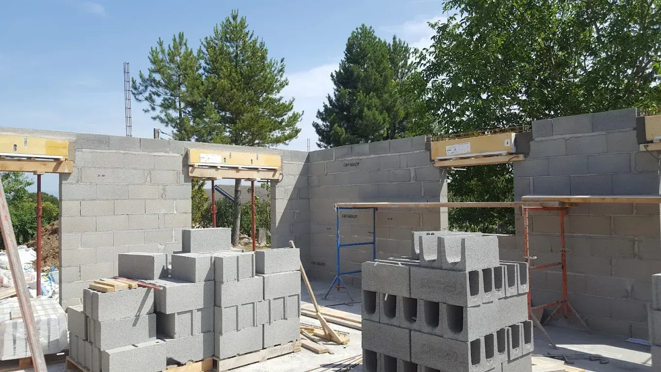Murs en parpaings partiellement construits sur un chantier, avec des blocs empilés et des arbres en arrière-plan.