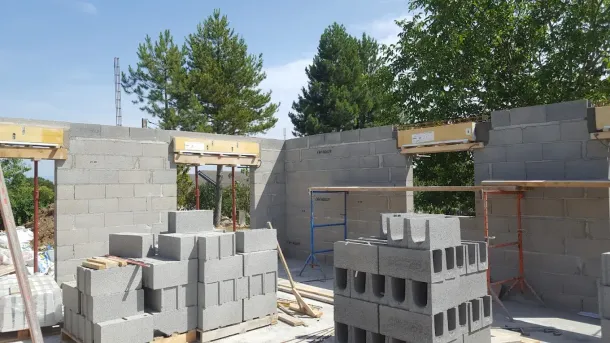 Murs en parpaings d'un bâtiment en construction, avec des linteaux en bois au-dessus des portes et des piles de parpaings.