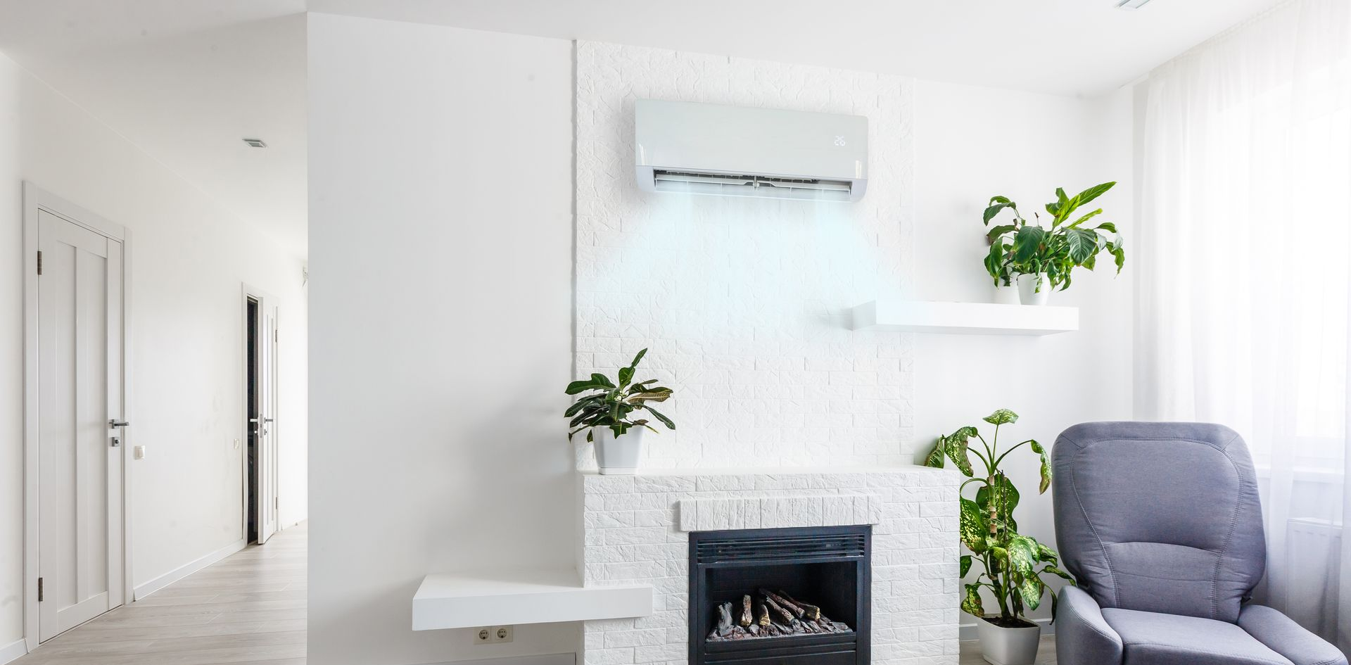 Salon minimaliste lumineux avec murs blancs, cheminée, plantes et fauteuil gris