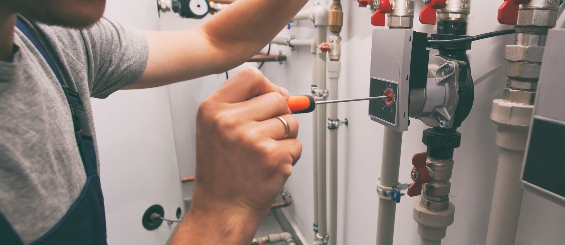 Une personne serre une vanne sur une installation de plomberie industrielle avec un tournevis.