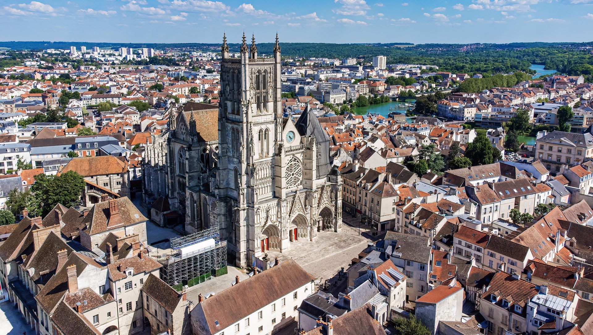 Vue aérienne d'une cathédrale gothique dominant un paysage urbain historique aux toits rouges denses.