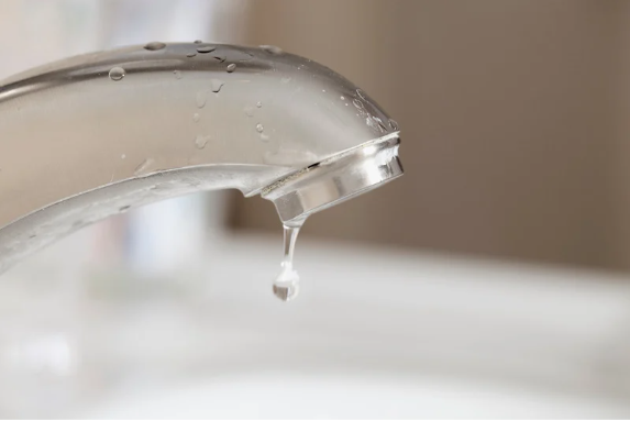 Un tuyau blanc qui fuit laisse couler de l'eau dans un seau sous l'évier.