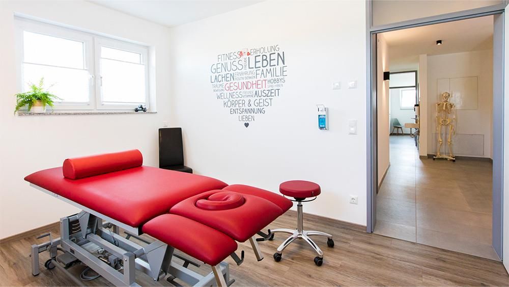 Eine rote Massageliege in einem Raum mit einem Herz an der Wand.