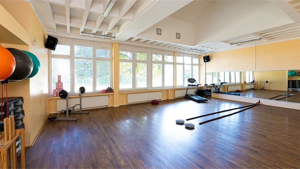 Ein großer leerer Fitnessraum mit Holzboden und einem großen Spiegel.