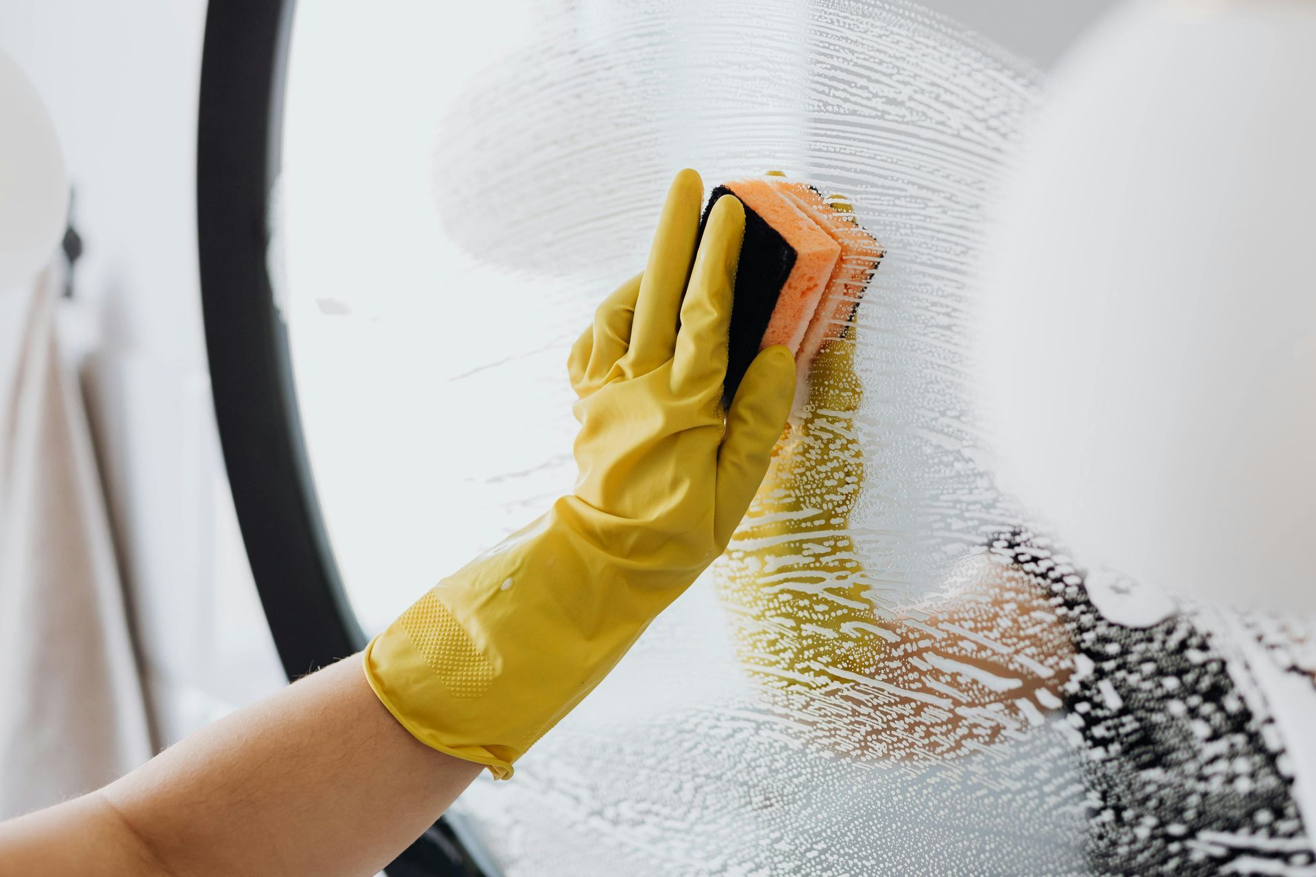 Una persona que lleva guantes amarillos está limpiando una ventana con una esponja.