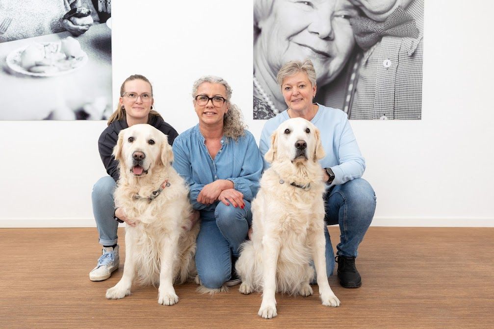 Mitarbeiterinnen Olia: Drei Frauen sitzen neben zwei Hunden auf einem Holzboden.