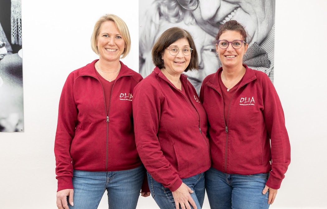 Mitarbeiterinnen Olia: Drei Frauen in roten Jacken und Jeans posieren für ein Foto.