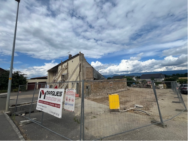 Chantier : bâtiment partiellement démoli derrière une clôture métallique, ciel nuageux au-dessus.