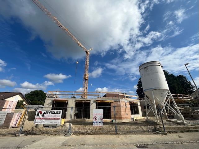 Chantier de construction avec une grue, un silo en béton et un bâtiment en construction contre un ciel bleu.