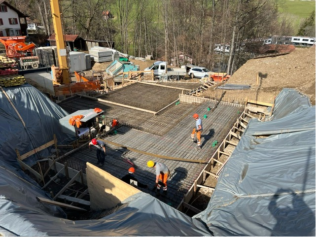 Chantier de construction : des ouvriers en gilet orange construisent des fondations en béton à l'extérieur.