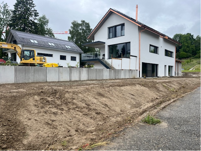 Maisons blanches modernes avec un chantier de construction devant, une excavatrice et un mur de soutènement visibles.