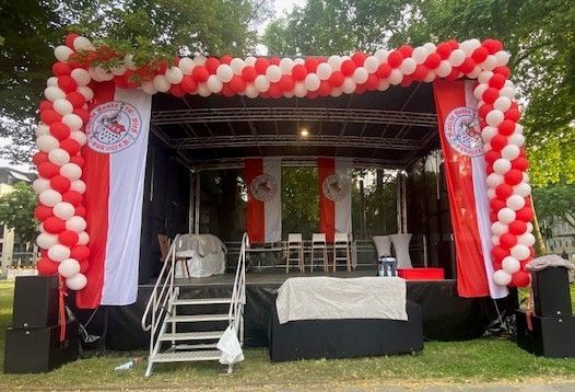 Auf einer Bühne mit roten und weißen Luftballons und einer Fahne