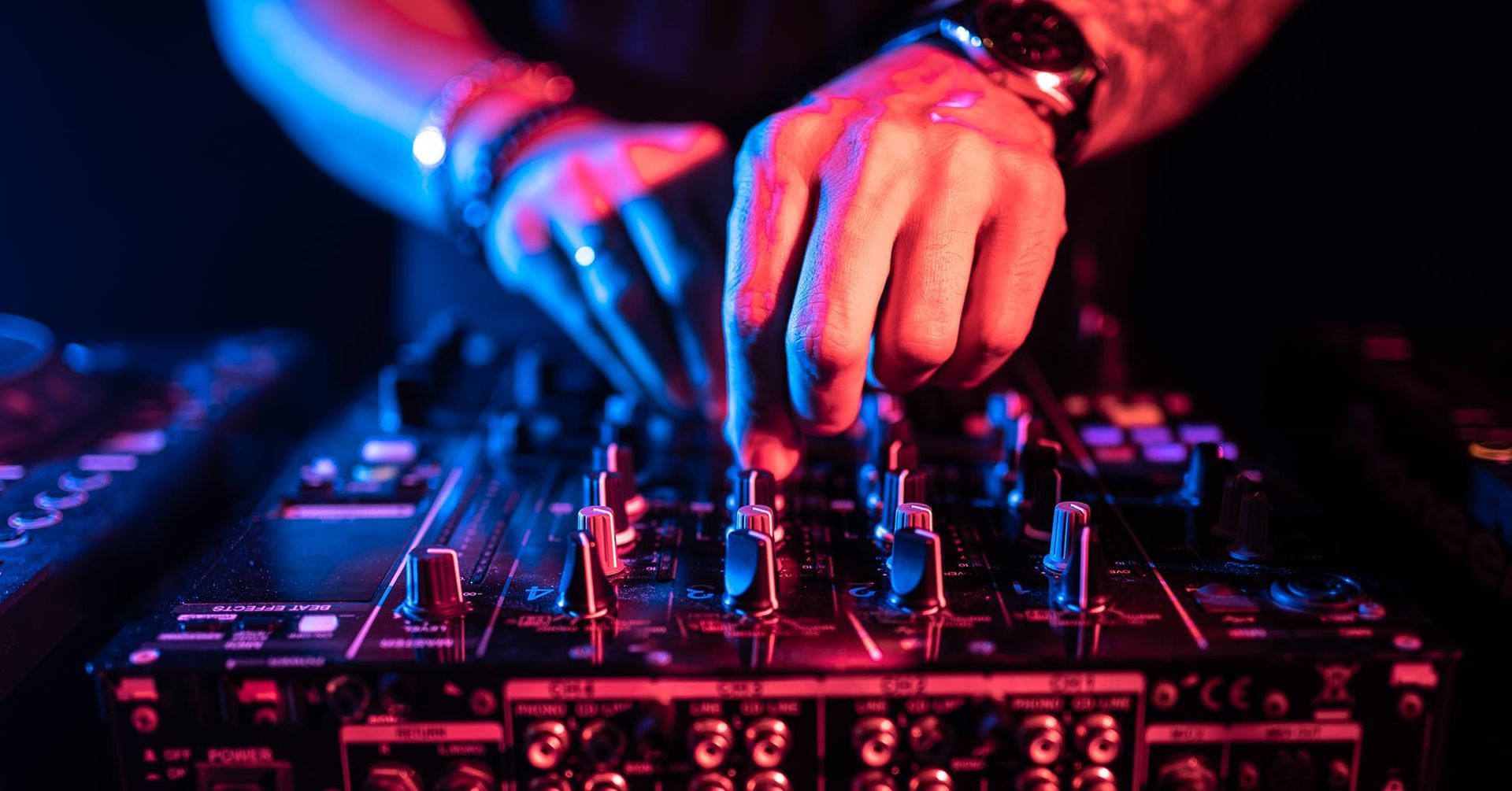 Hände verstellen Regler an einem DJ-Mixer unter rosa und blauer Clubbeleuchtung