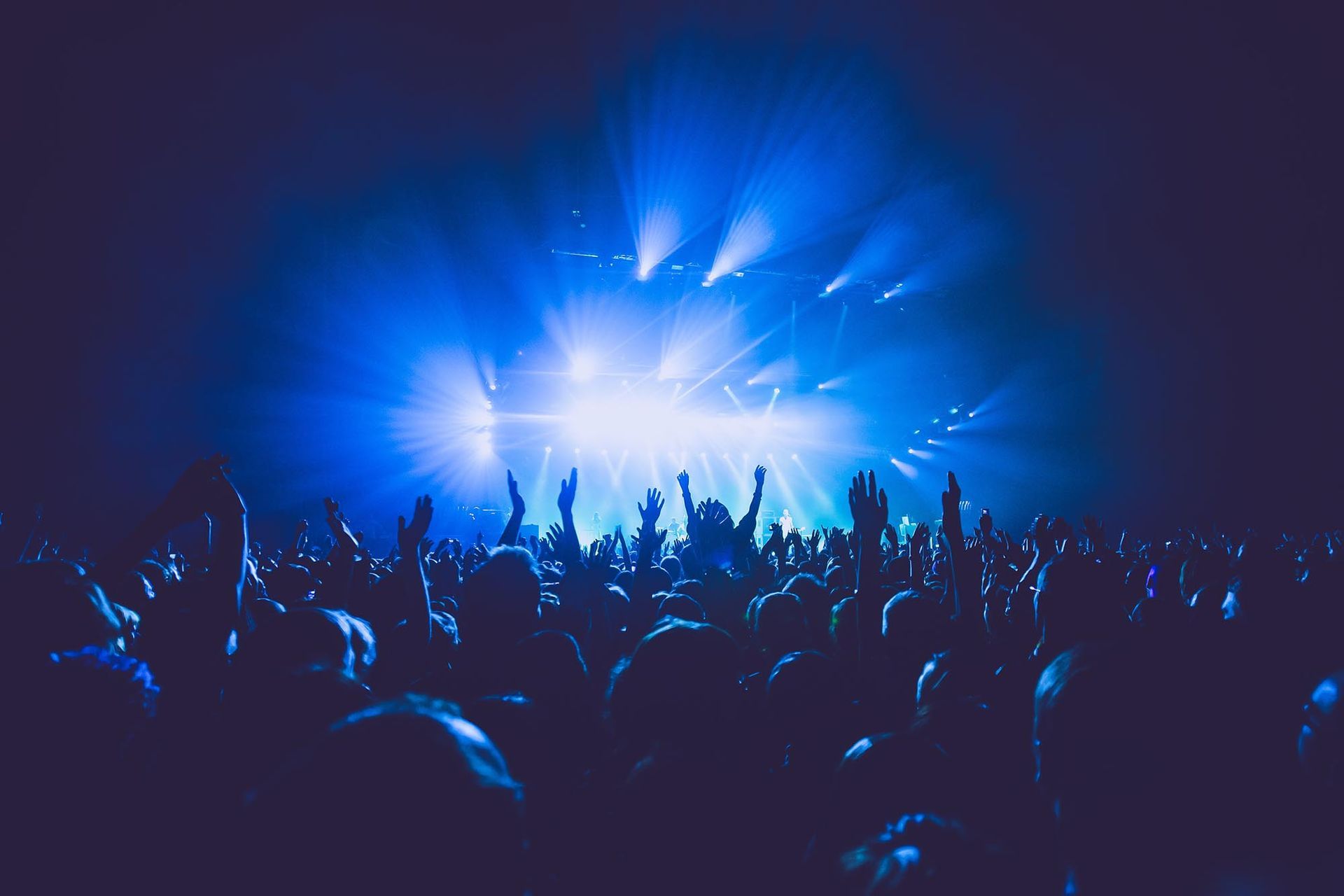 Eine Menschenmenge tanzt bei einem blau beleuchteten Konzert mit erhobenen Händen und hellem Bühnenlicht.