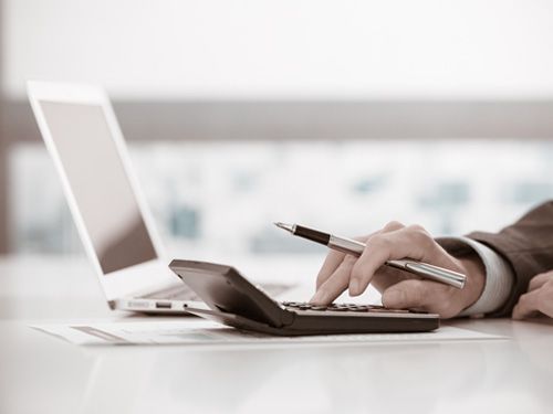 Una persona está usando una calculadora y un bolígrafo frente a una computadora portátil.