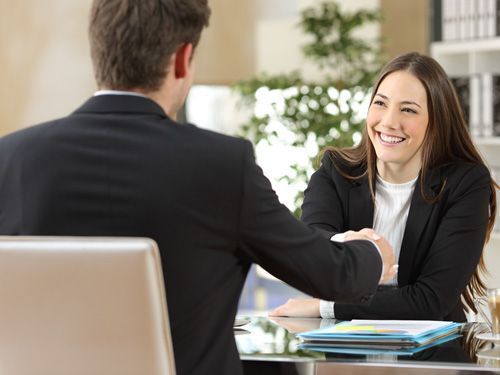 Una mujer le estrecha la mano a un hombre durante una entrevista de trabajo.