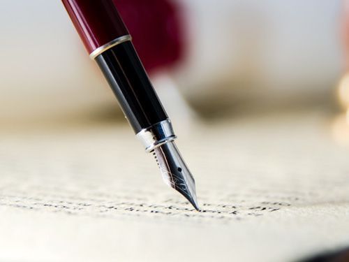 Una persona está escribiendo con una pluma fuente en un trozo de papel.