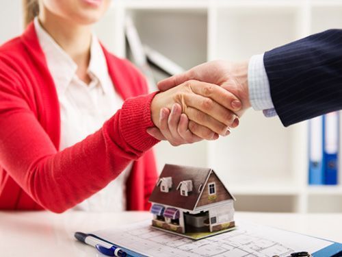 Un hombre y una mujer se dan la mano sobre una casa modelo.