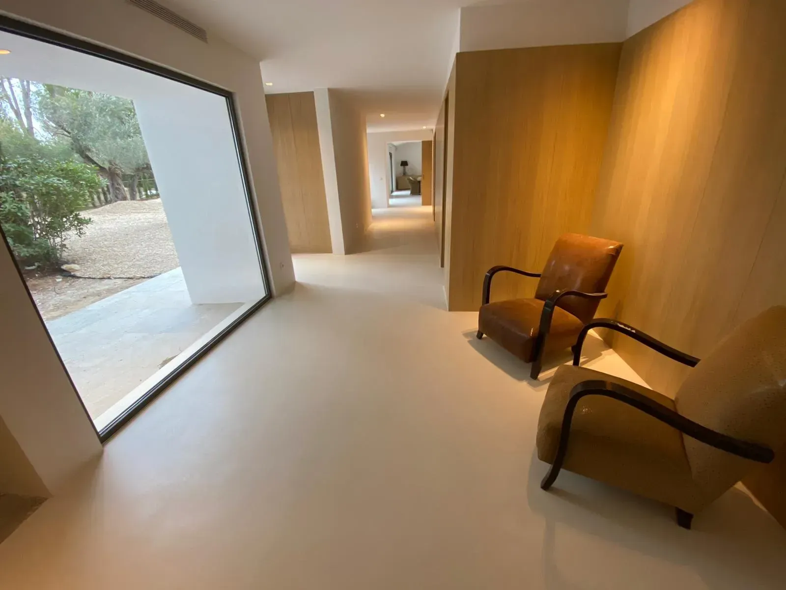 Pasillo con dos sillas color canela, gran ventanal y paredes de color claro.