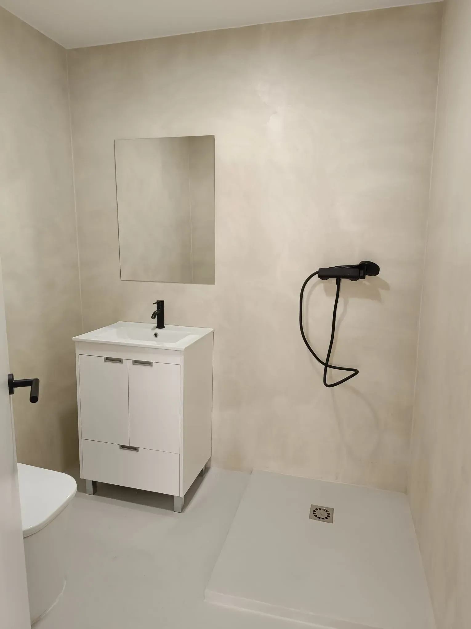 Pequeño baño moderno con mueble de lavabo blanco, ducha y paredes texturizadas de color beige.