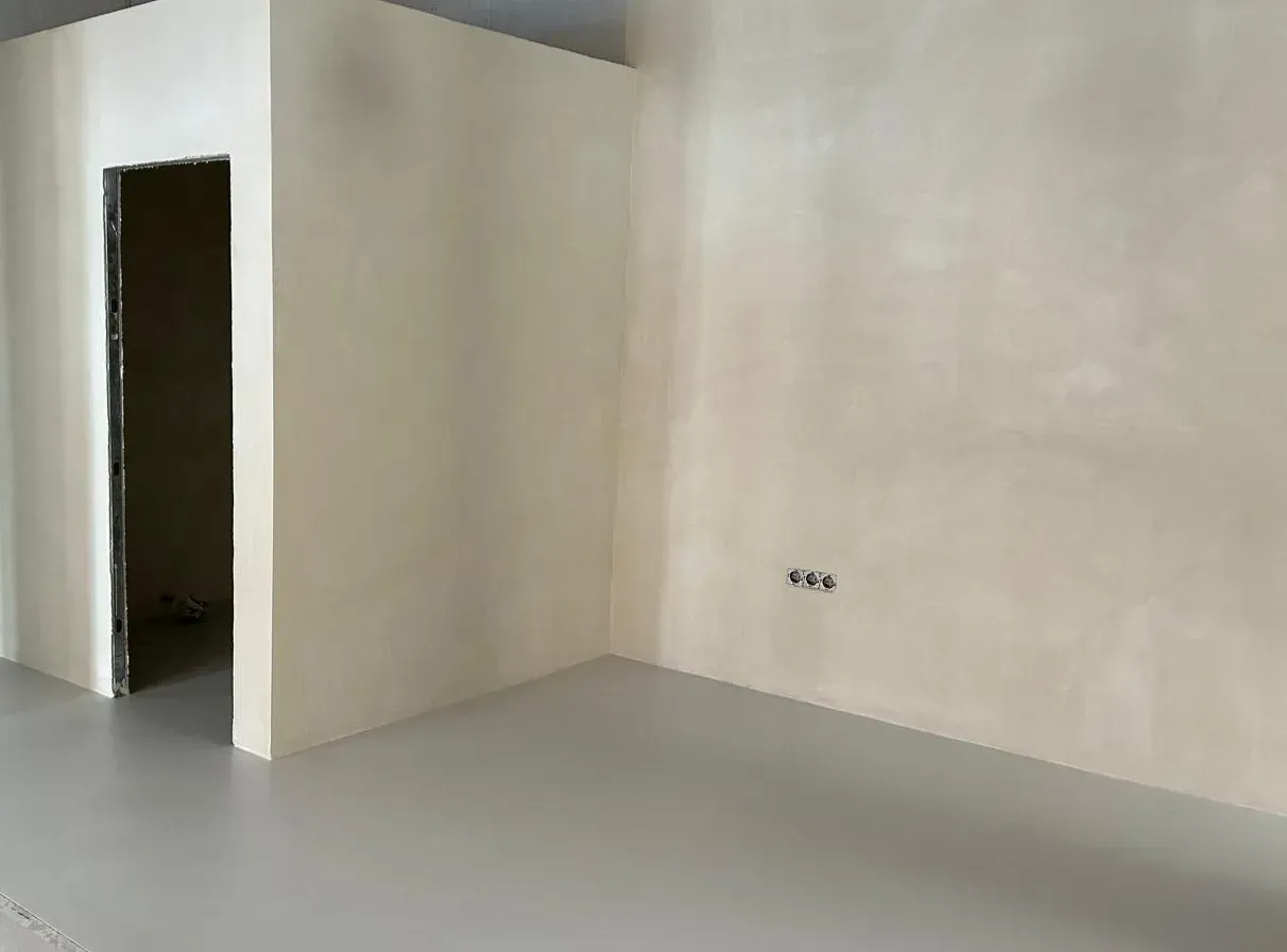 Habitación vacía con suelo gris, paredes beige y una puerta abierta.