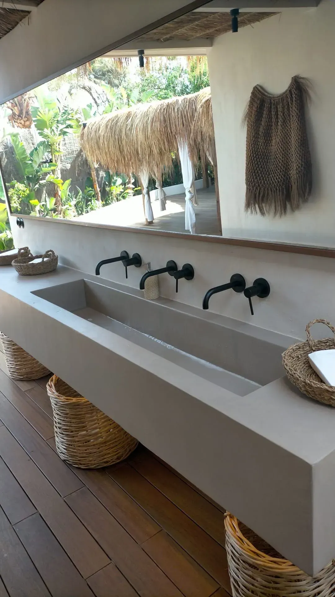 Fregadero exterior con tres grifos negros, integrado en una encimera de hormigón. Cestas debajo.