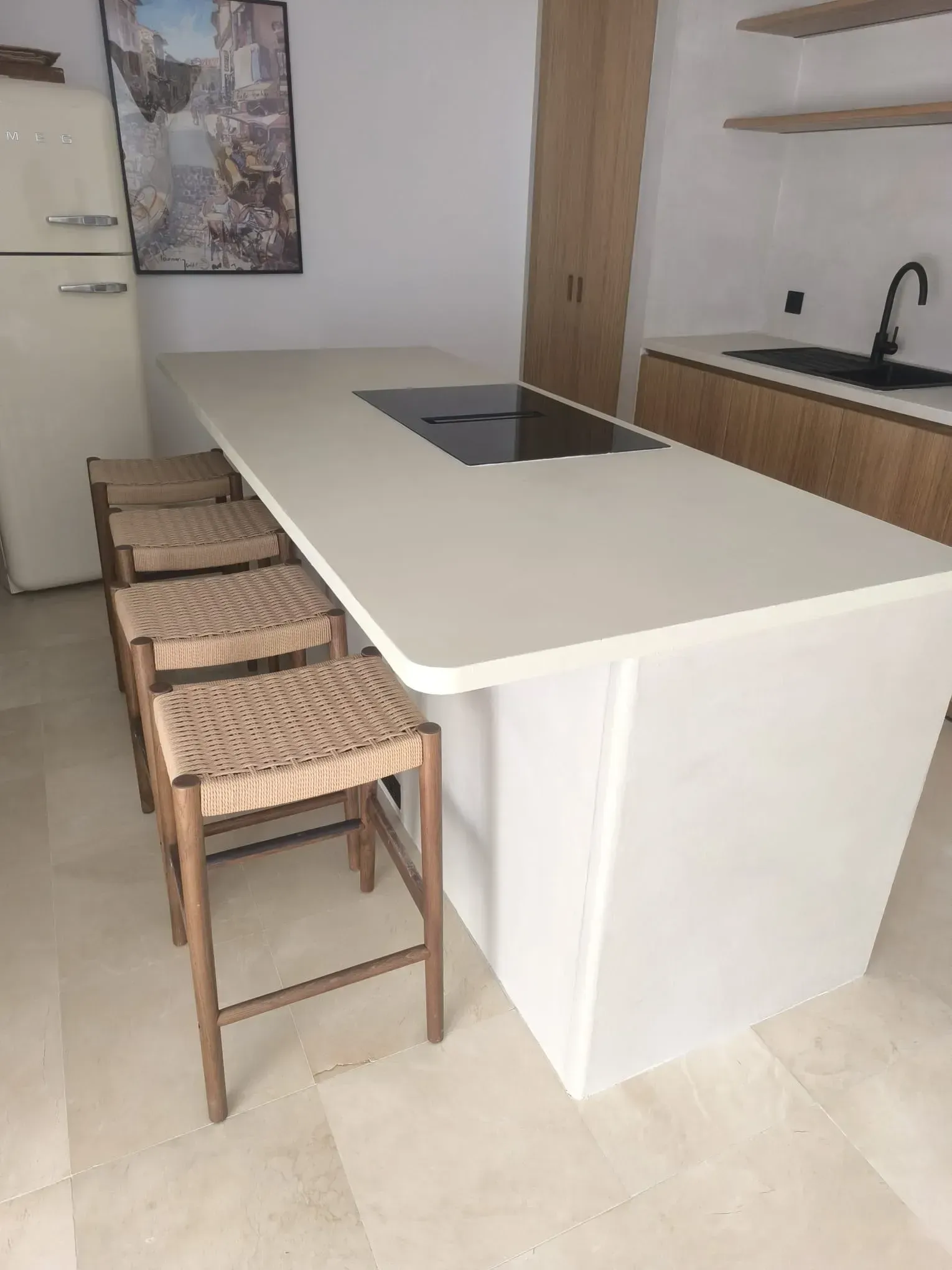 Cocina moderna con isla blanca, zona de estar y placa de cocina integrada. Taburetes de bar de tela.