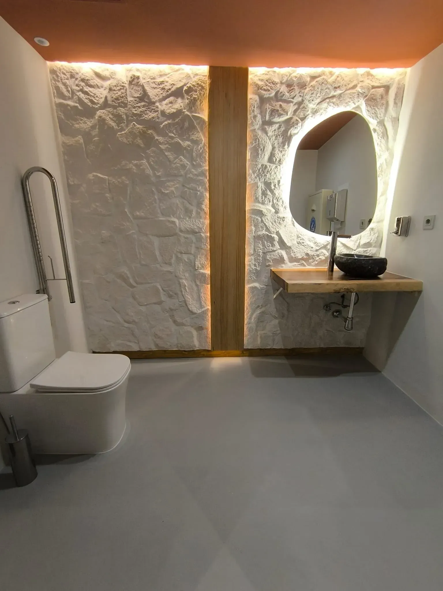 Baño moderno con pared texturizada, lavabo flotante e inodoro; suelo gris.